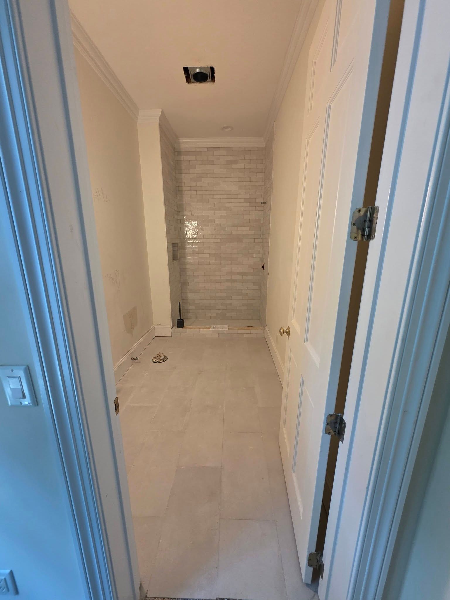 Narrow hallway under construction with white walls, tiled floor, and a tiled shower area at the end.