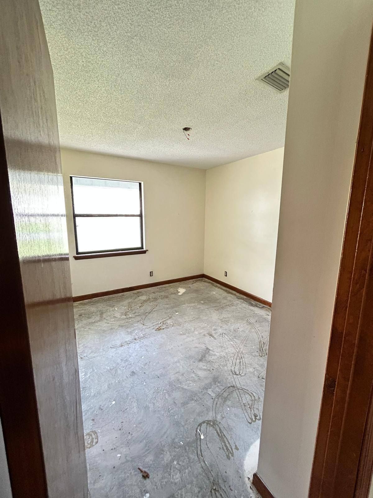 Empty beige room with a window, worn carpet, and wood trim viewed from the doorway