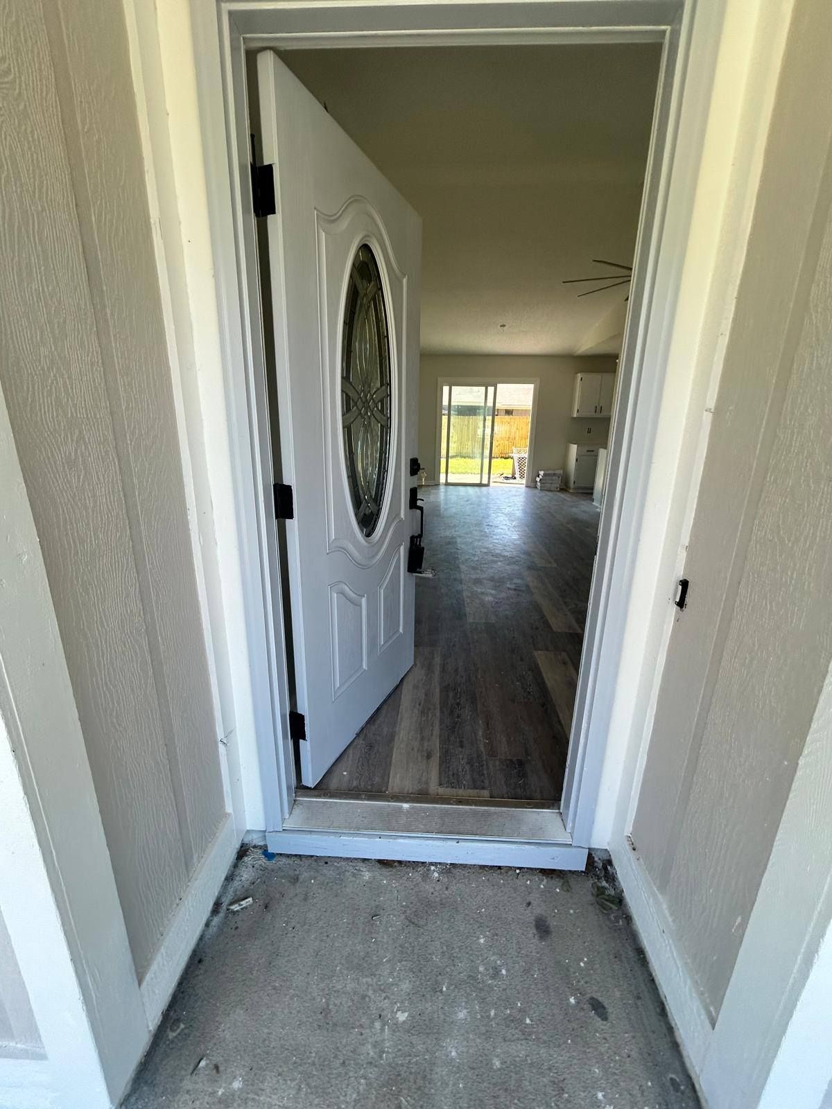 Open front door leading into a bright hallway with wood-look flooring.