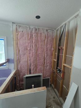 Partially demolished hallway with exposed studs, insulation, and drywall panels in a renovation site