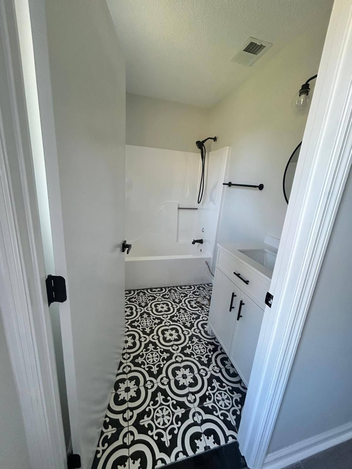 Narrow white bathroom with black-and-white patterned floor, bathtub, toilet, and vanity.