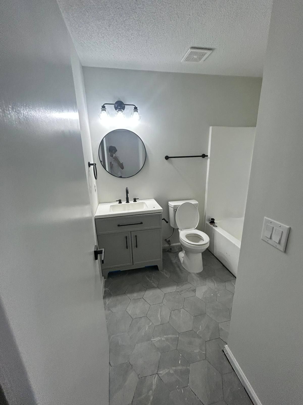 Small white bathroom with vanity, round mirror, toilet, and towel bar.