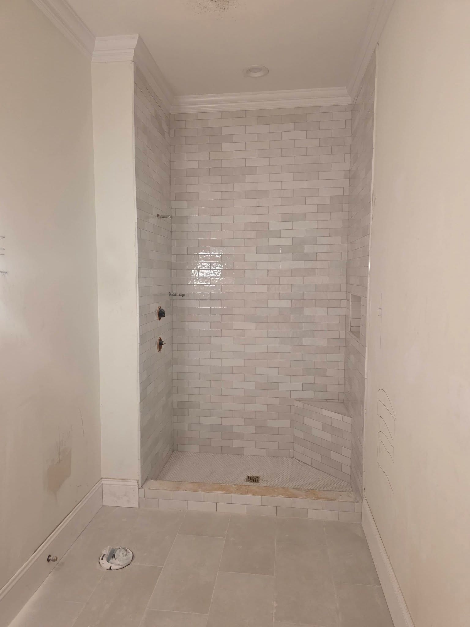 Empty bathroom alcove with tiled shower stall and white walls, unfinished floor