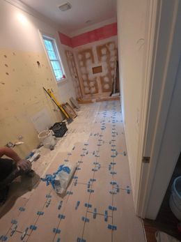 Renovated room with bare walls, floor protection, tools, and unfinished patching on the back wall