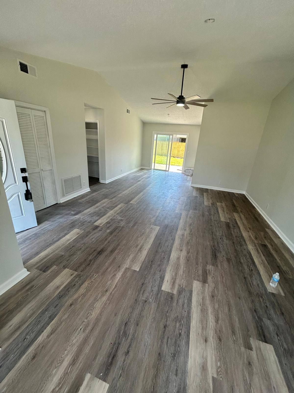 Empty living room with wood-look flooring, white walls, ceiling fan, and sliding glass doors.
