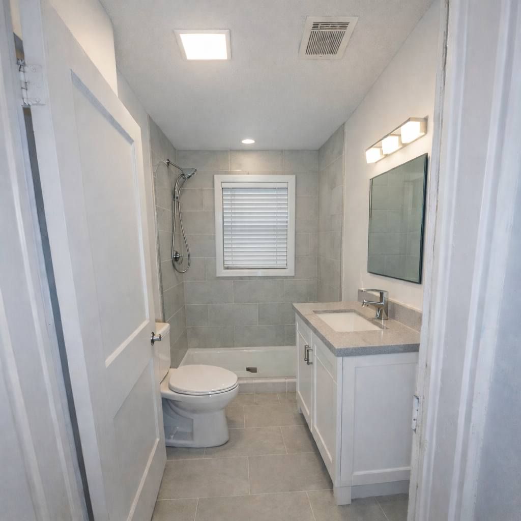 Small white bathroom with toilet, vanity, mirror, and shower window; clean modern interior.