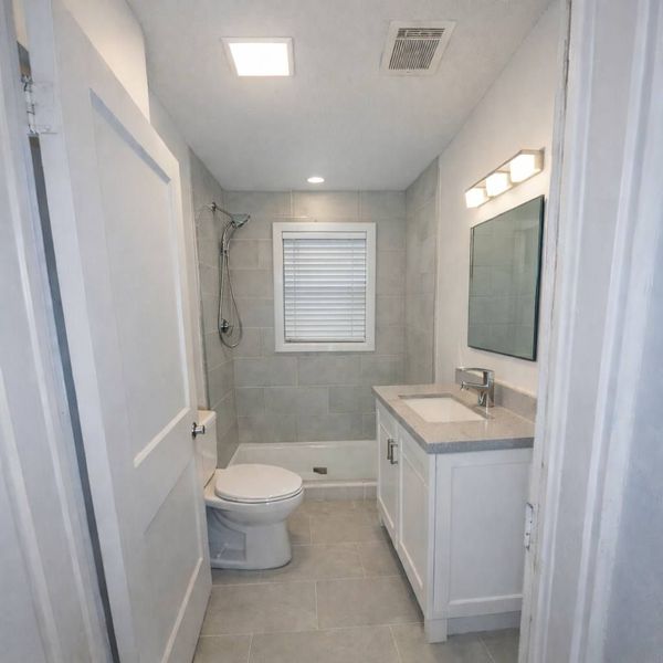 Small modern bathroom with toilet, vanity, mirror, shower, and tiled walls.