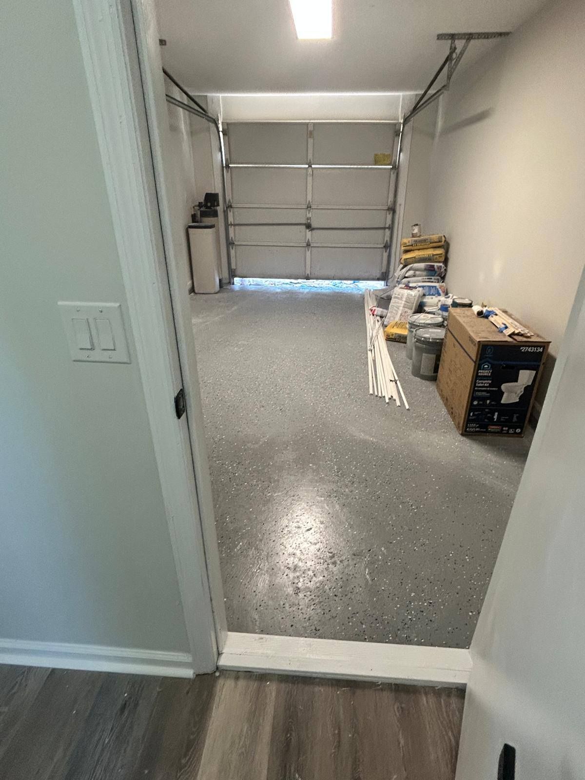 Open garage with speckled epoxy floor, closed garage door, and stacked supplies along the right wall.