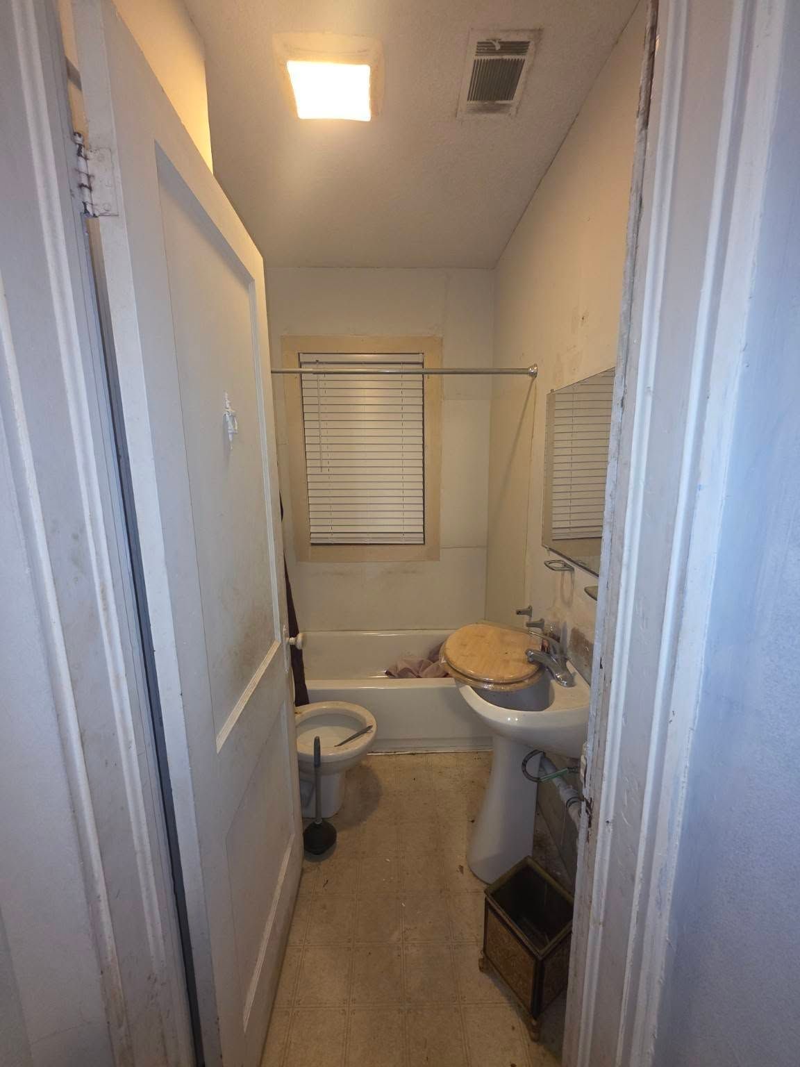 Narrow bathroom hallway with sink, toilet, and towel rack under a ceiling light