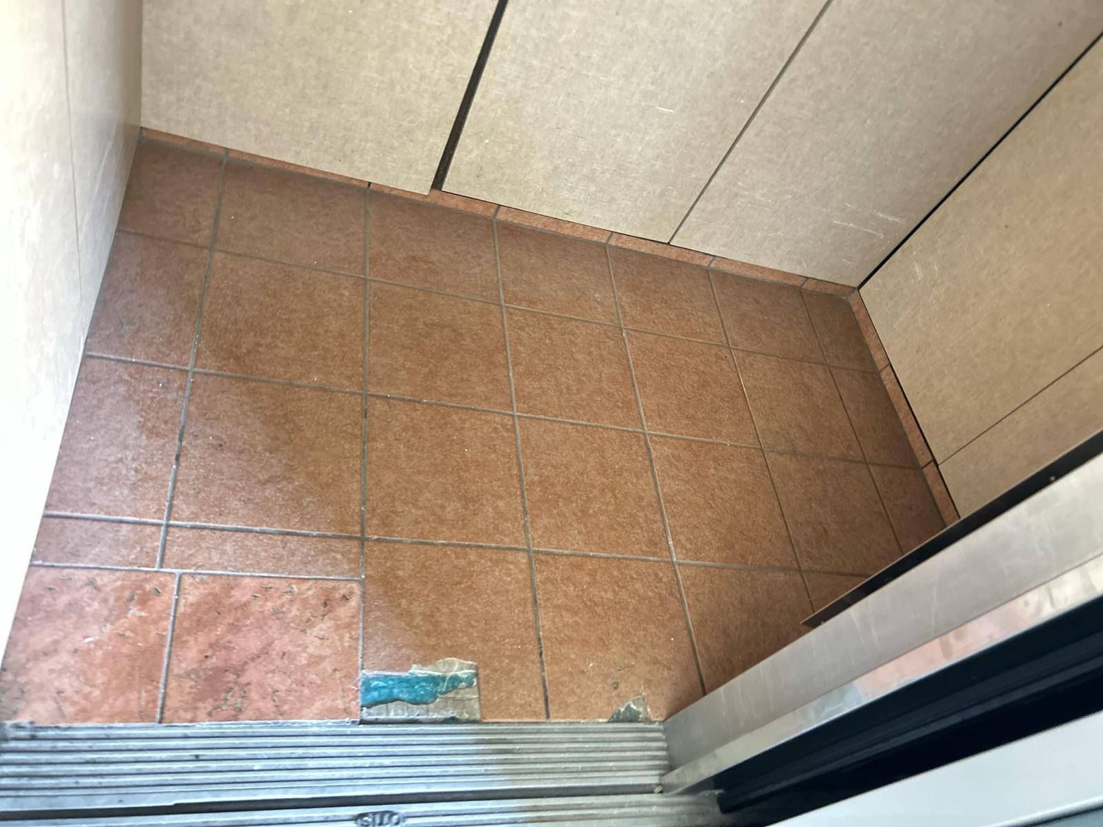 Empty tiled corner of a room with a sliding door and beige wall panels.