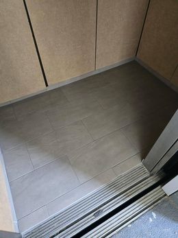 Open elevator with wood-paneled walls and gray tile floor, viewed from the doorway.