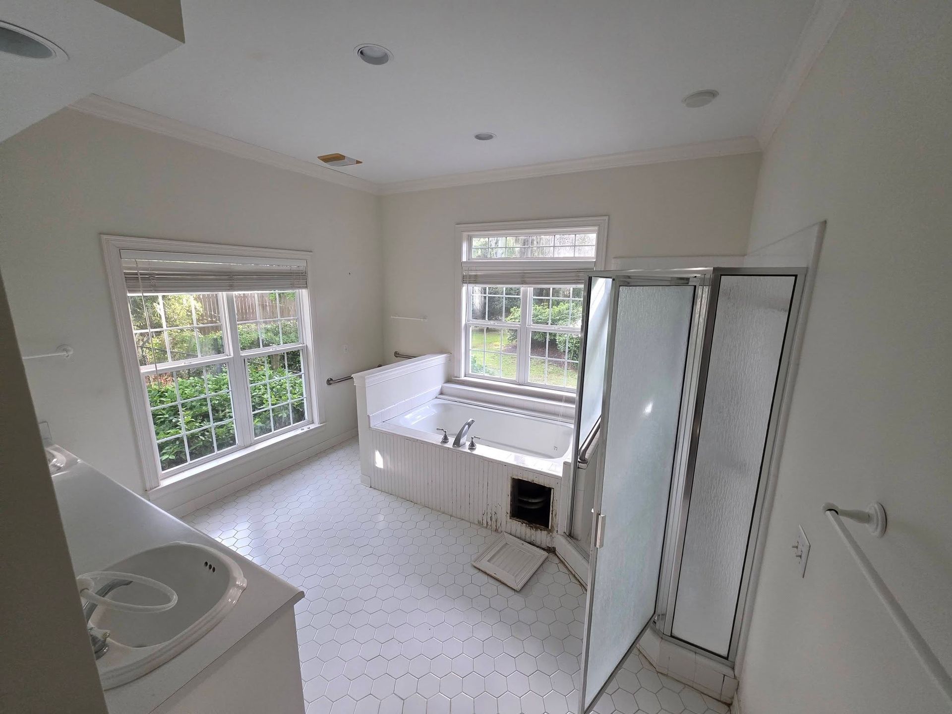 Bright bathroom with white vanity, bathtub, windows, and glass shower door