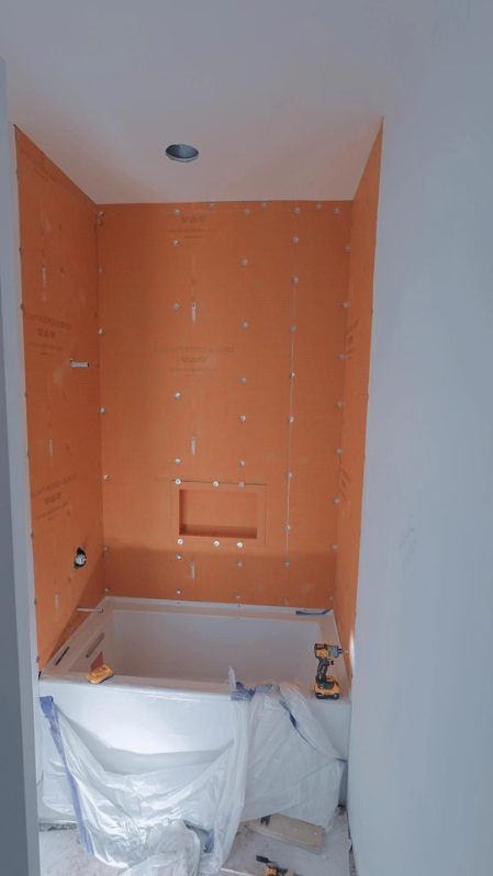 Small bathroom with orange tiled walls and a bathtub covered by a white protective sheet.