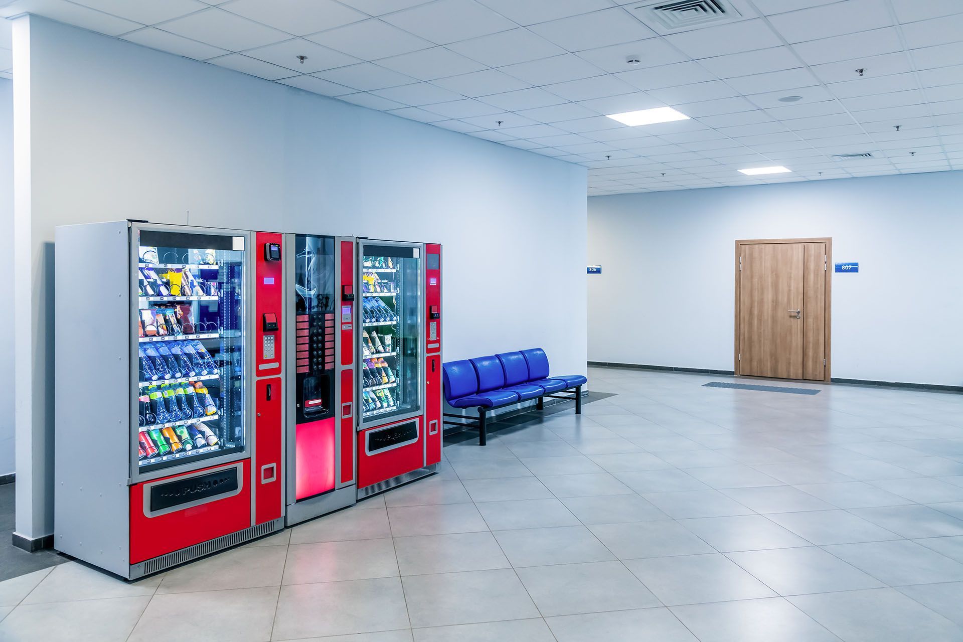 A group of red vending machines stands by the wall inside a public building, after installation.