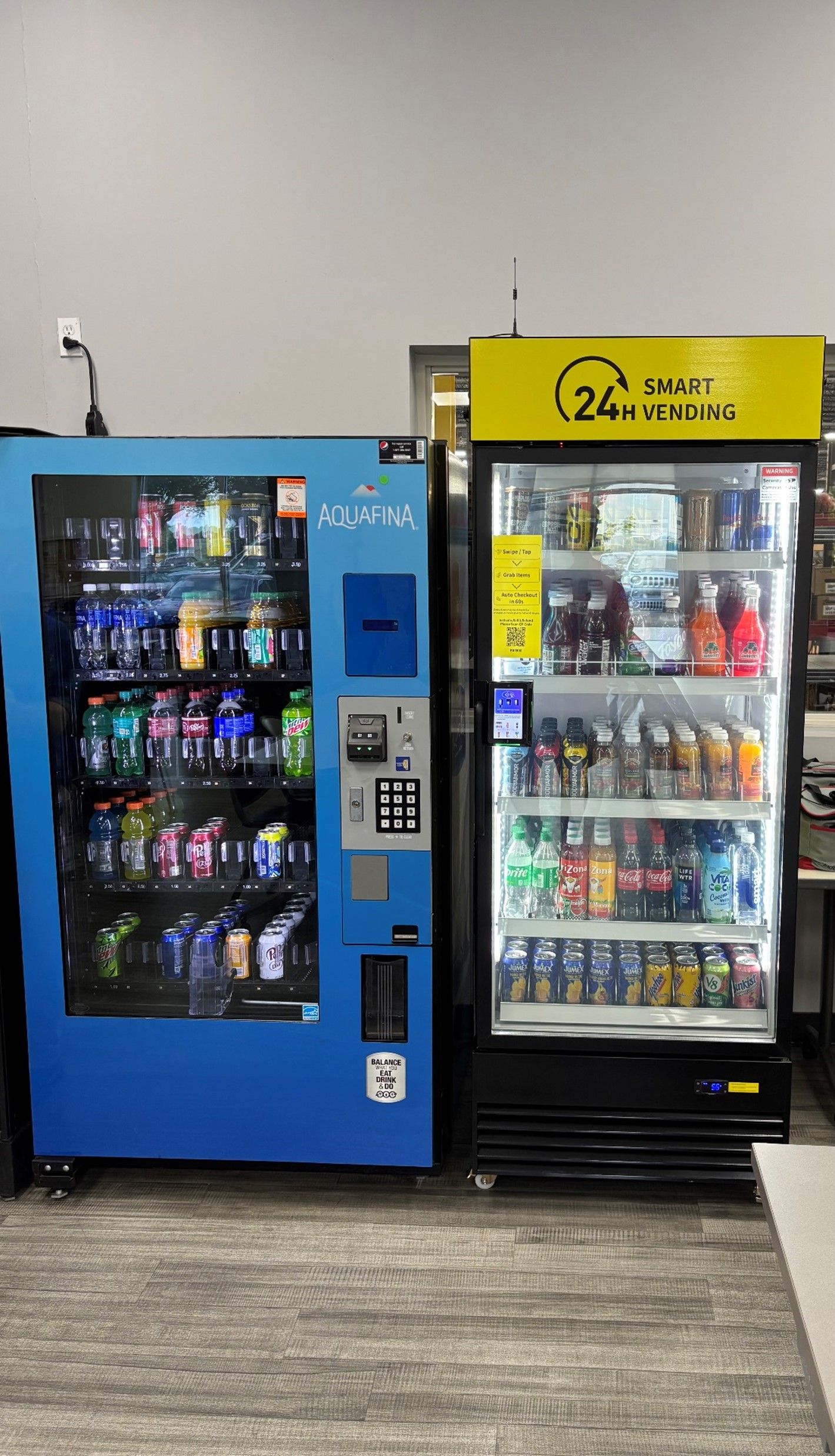 Two vending machines: a blue one with snacks and a black one with drinks, in an indoor setting.