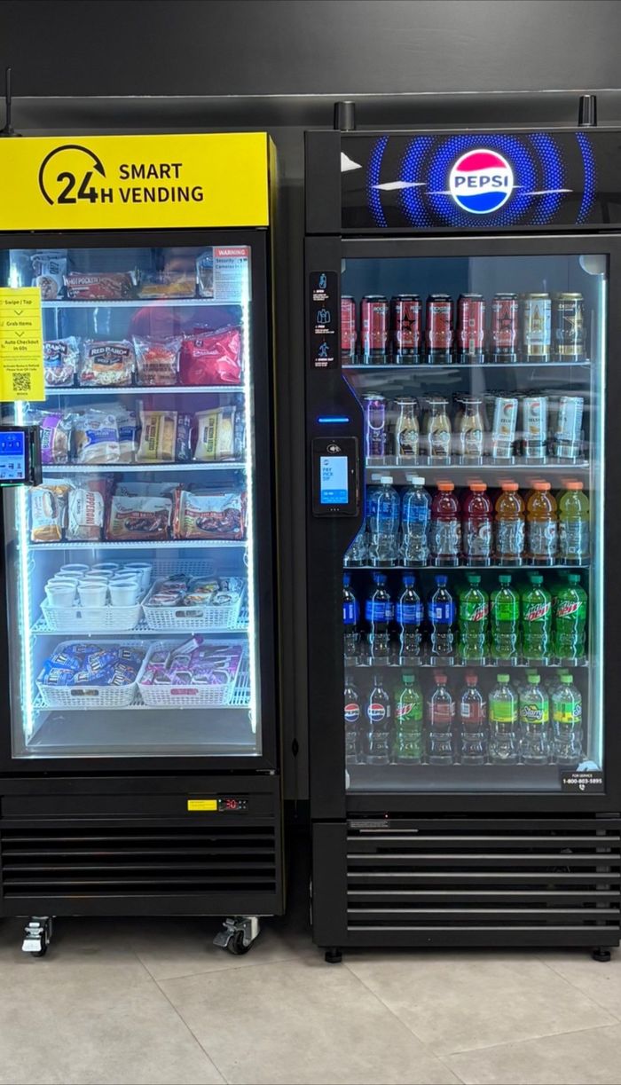 Two refrigerated vending machines; one yellow, one with a Pepsi logo, filled with food and drinks.