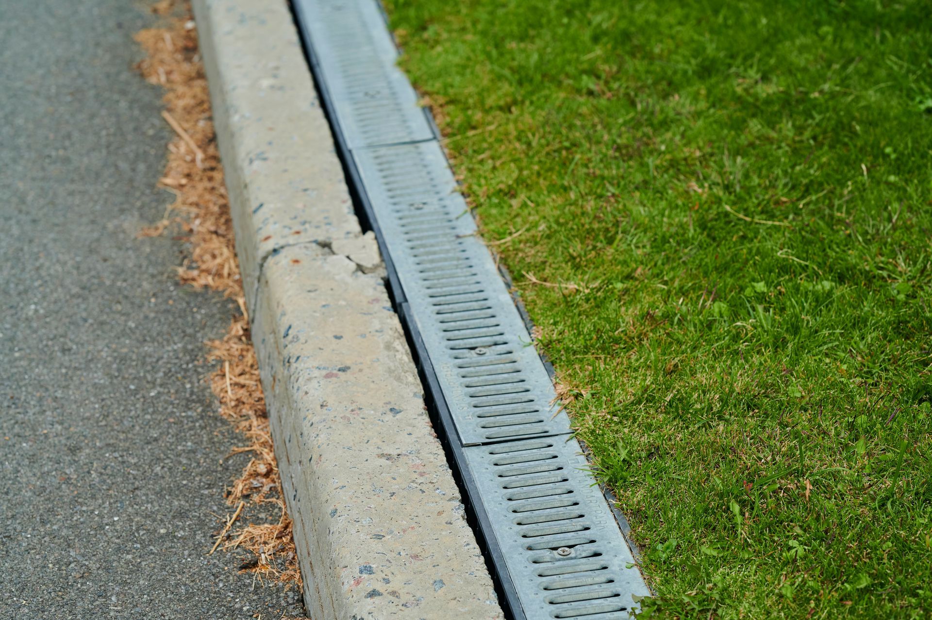 A drain on the side of a road next to a grassy area.