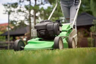 A woman is using a green lawn mower to cut the grass.