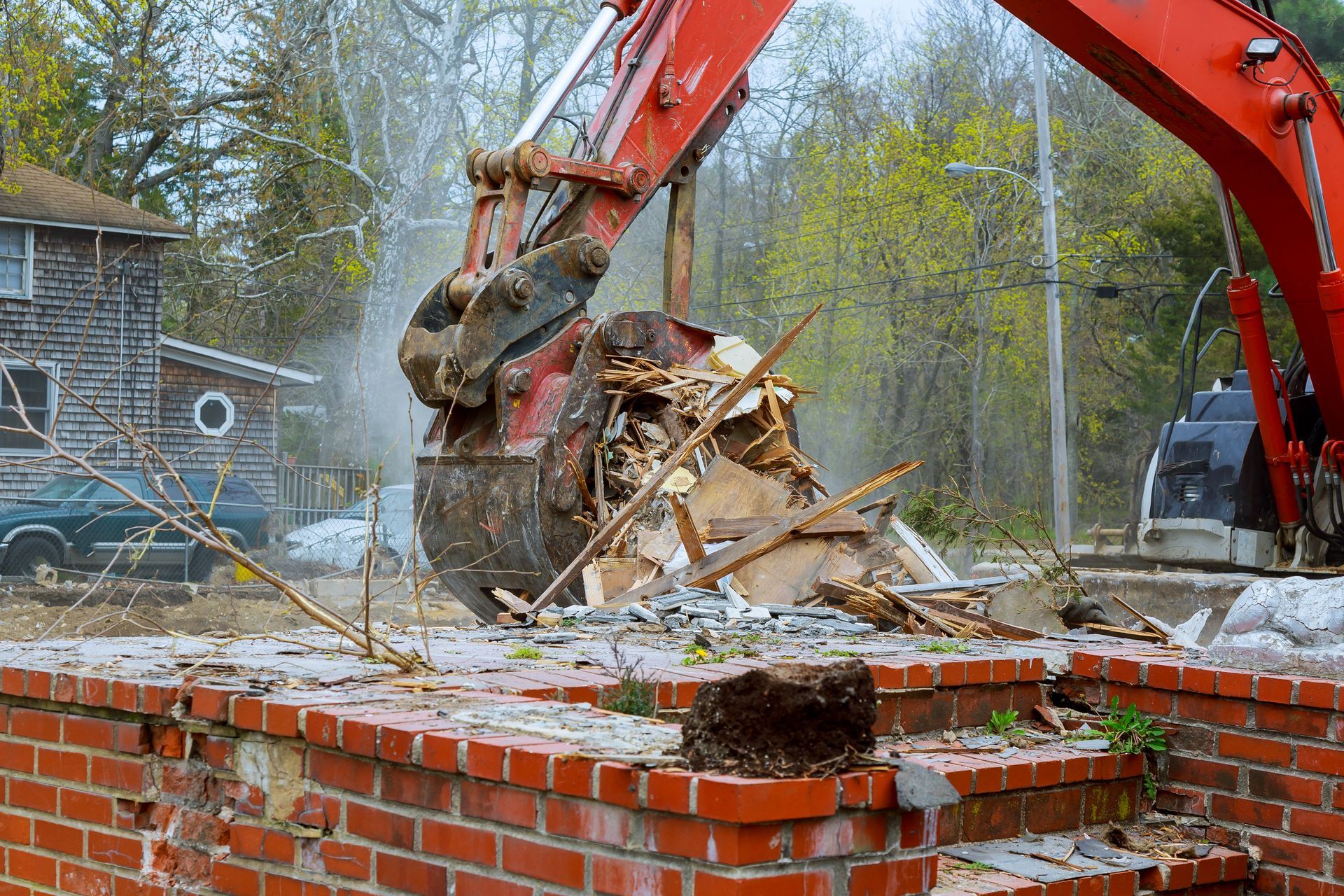 A red excavator is demolishing a brick wall.