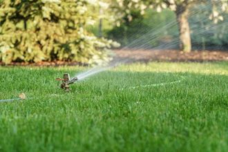 A lawn sprinkler is spraying water on a lush green lawn.