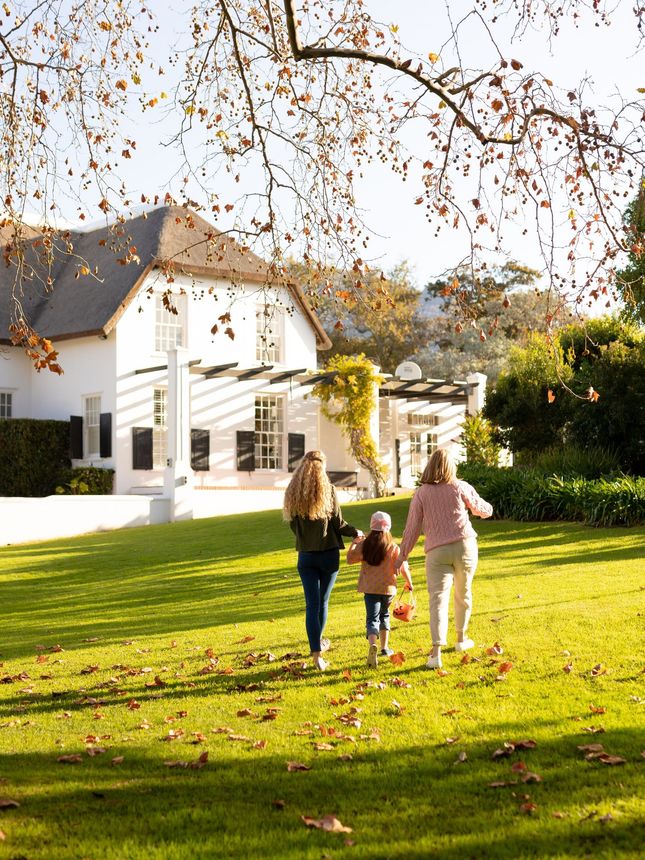 Three people are walking through a grassy field in front of a house.