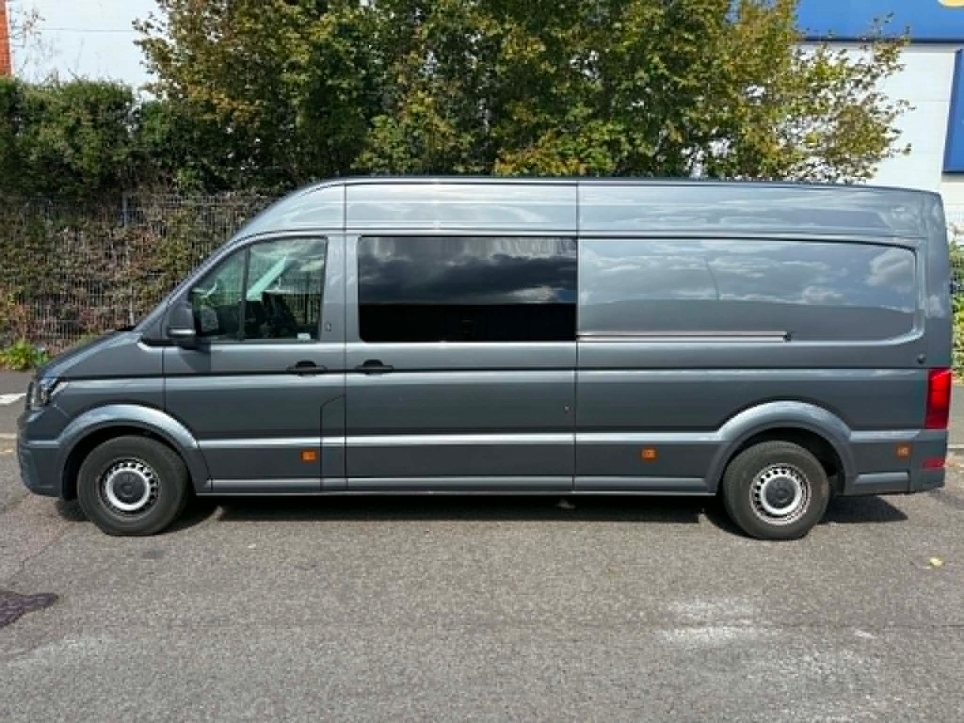 A gray van is parked in a parking lot in front of a red building.