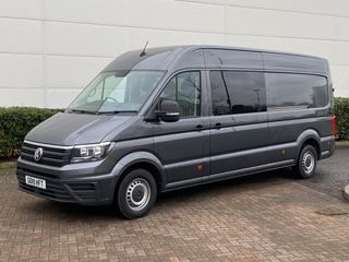 A gray van is parked in a parking lot in front of a red building.