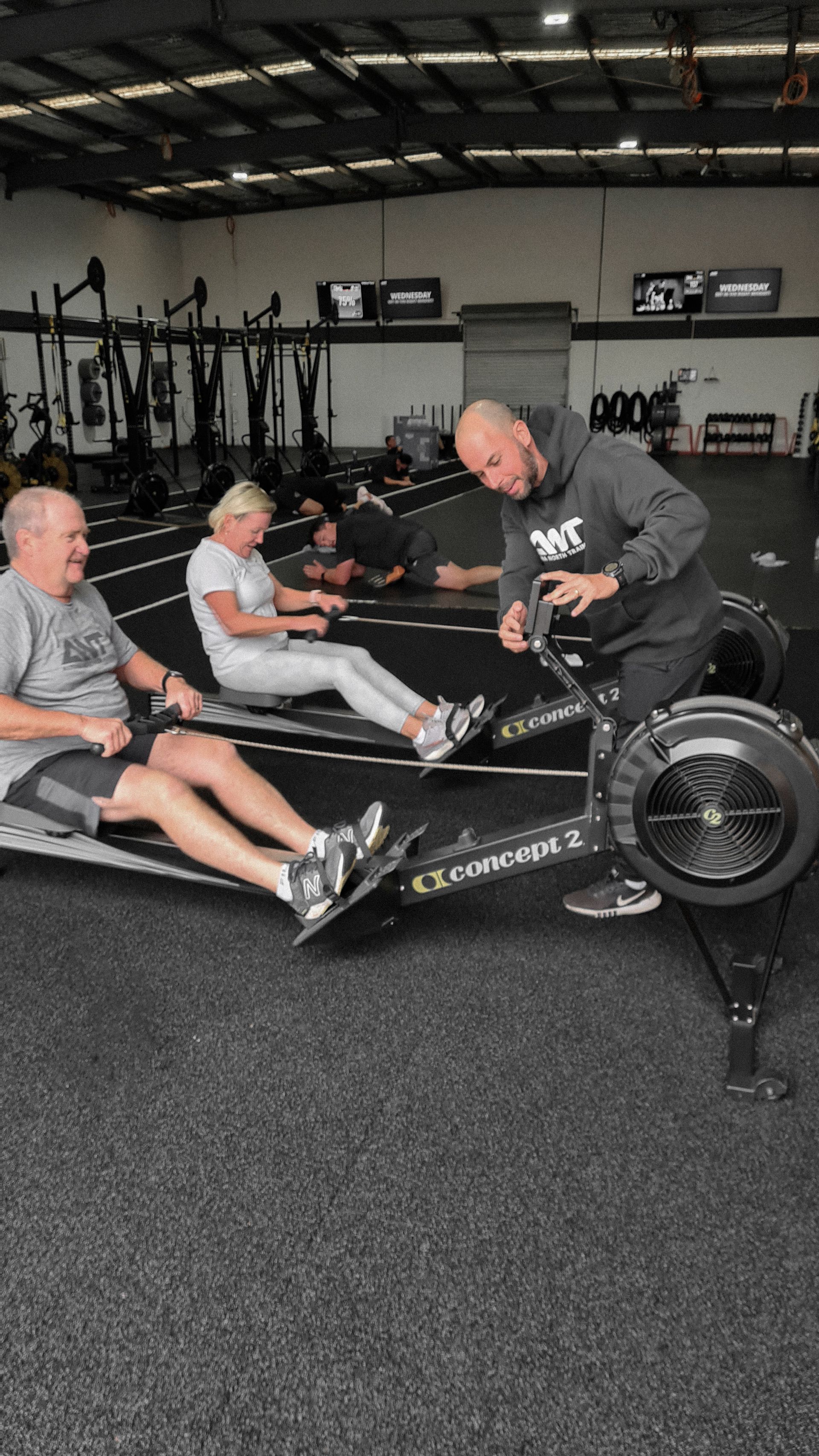 A group of people are sitting on rowing machines in a gym.
