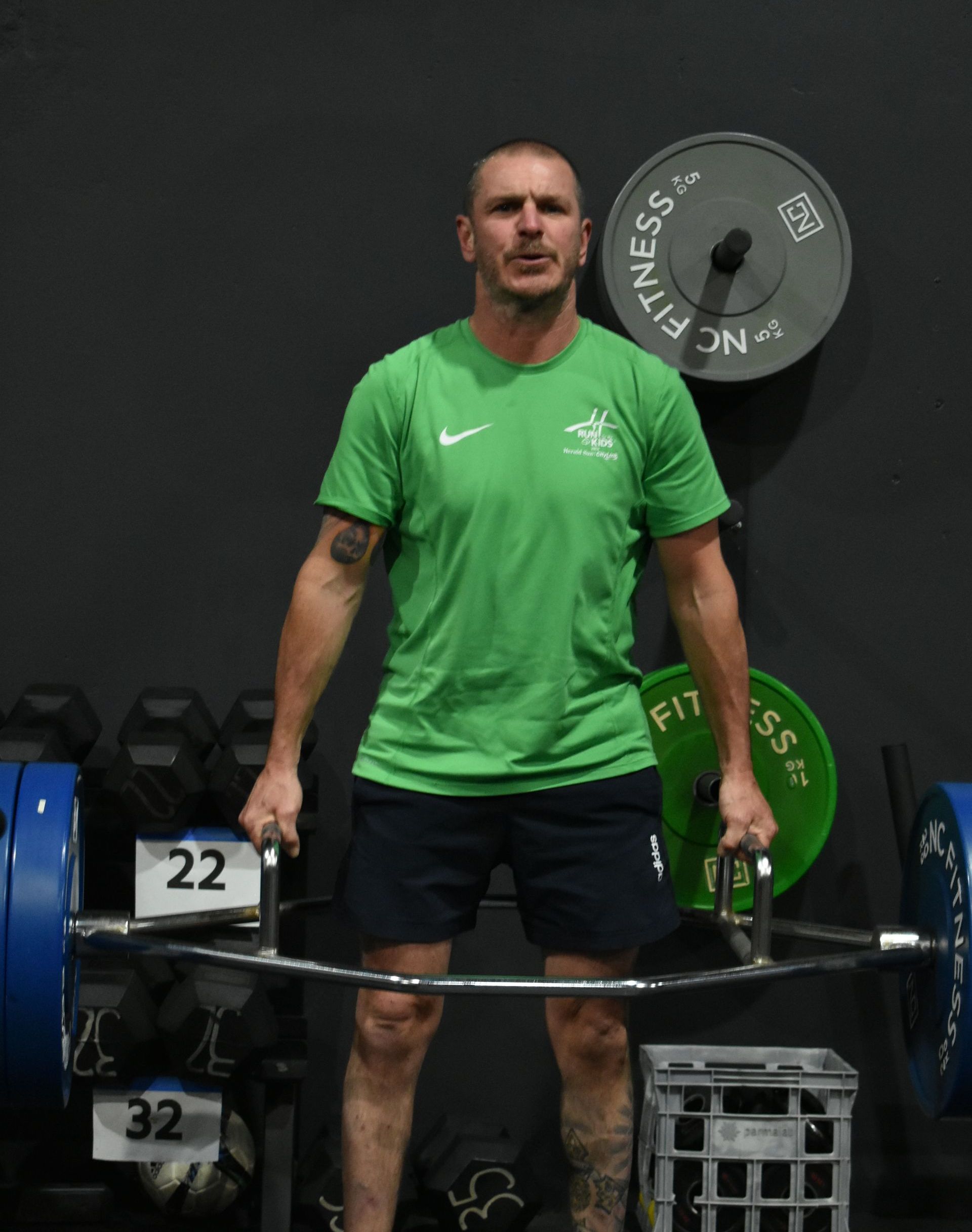 A man in a green shirt is lifting a barbell in a gym