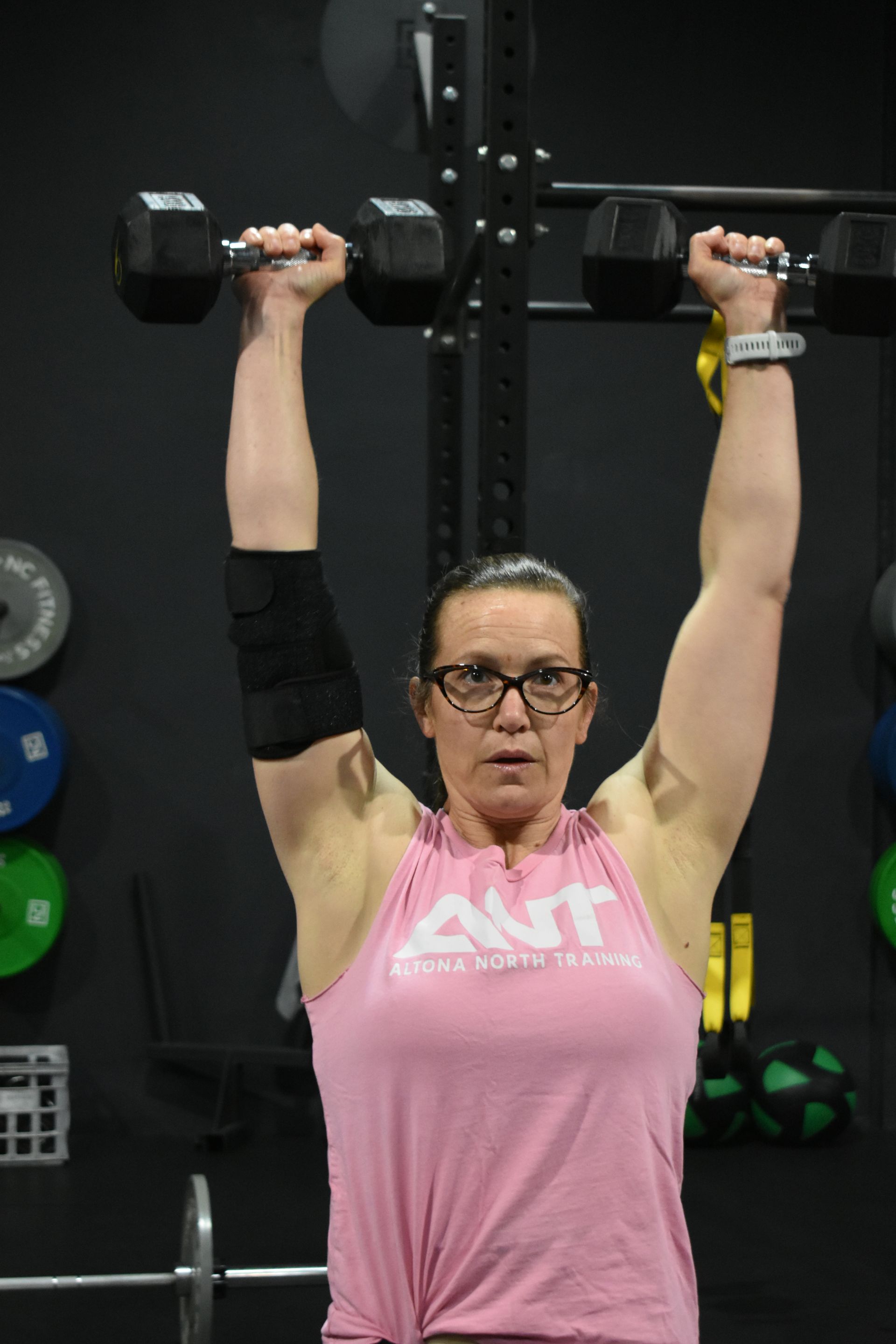 A woman is lifting a dumbbell over her head in a gym.