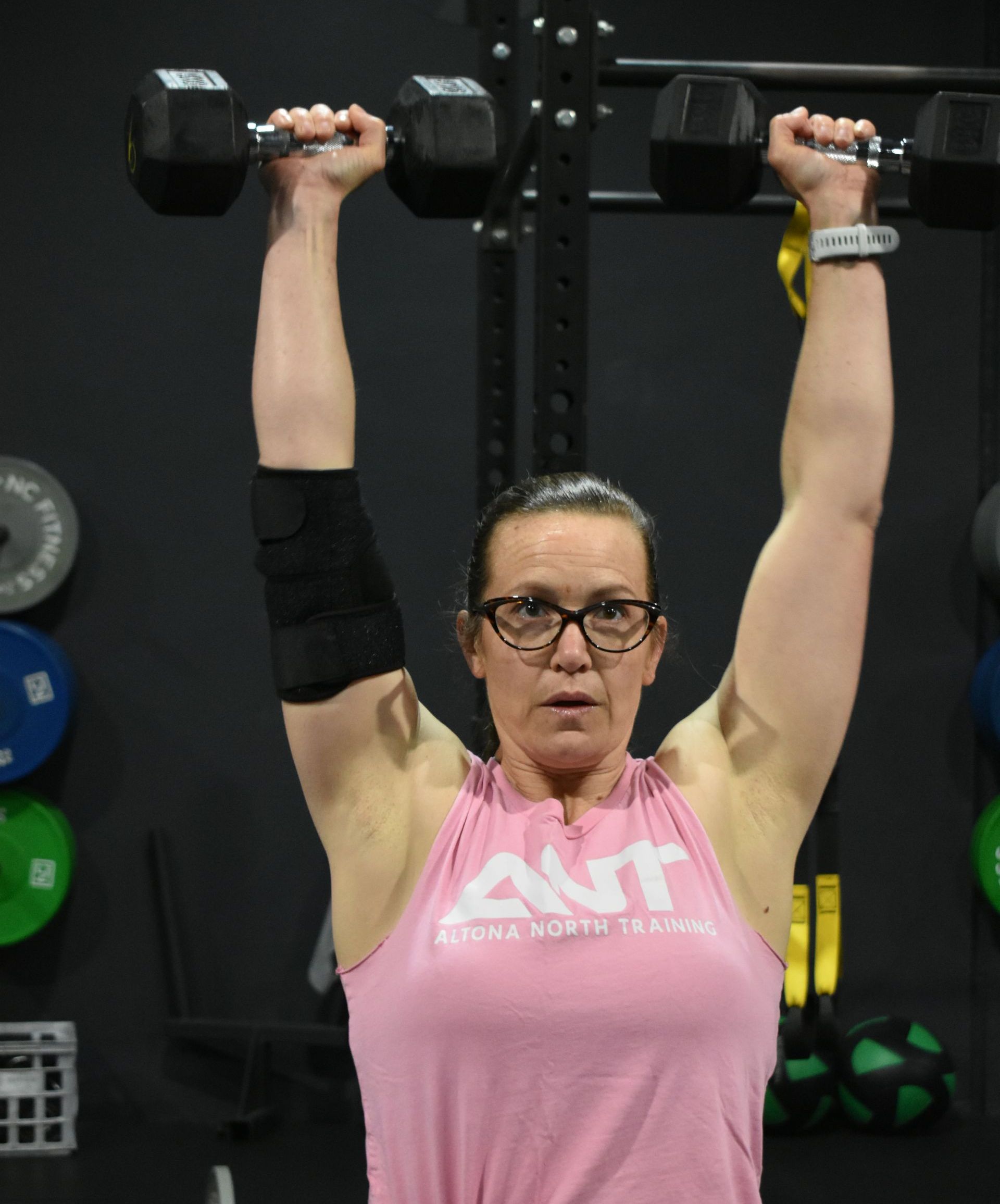 A woman in a pink ant tank top is lifting dumbbells over her head