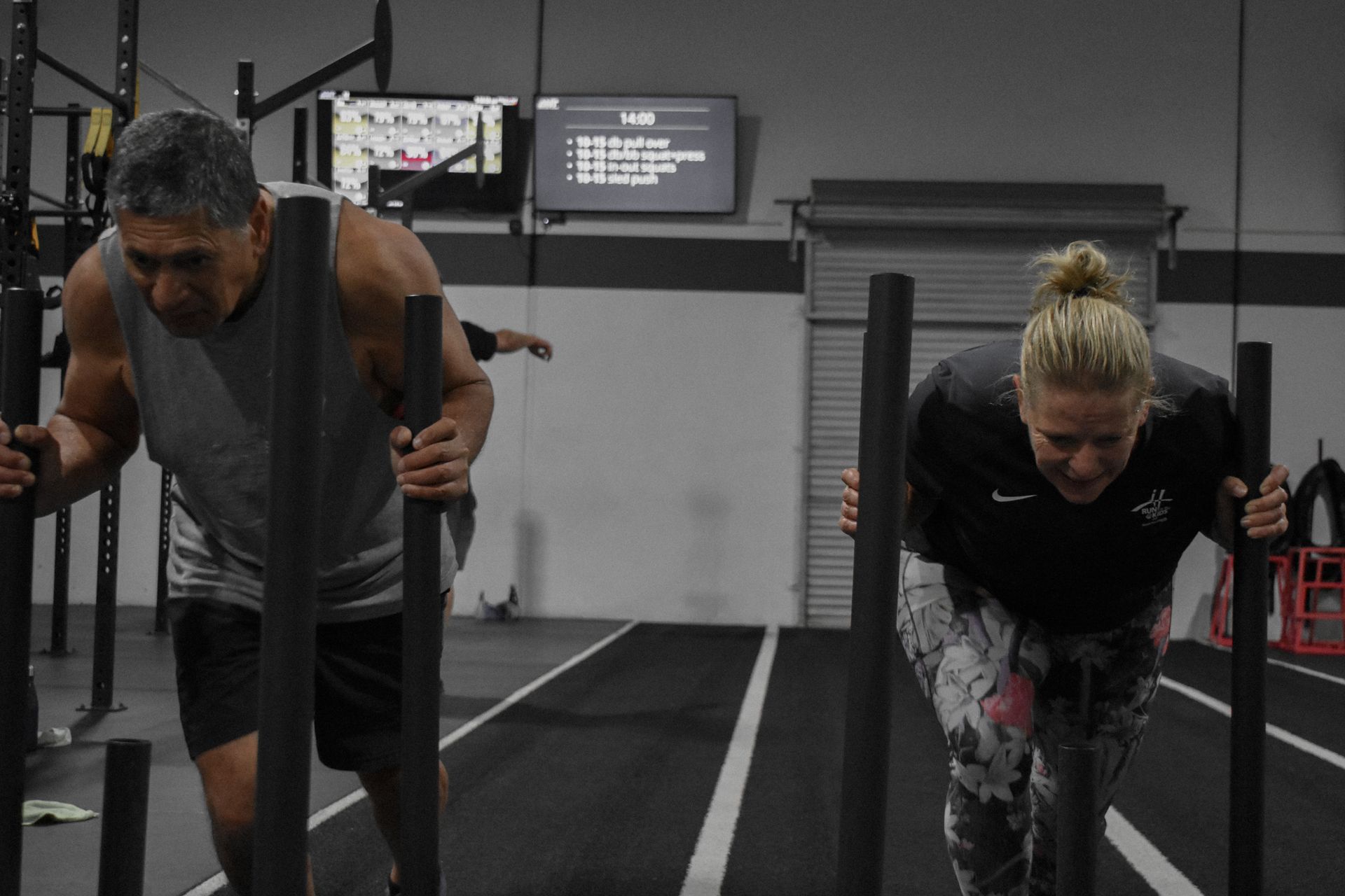 A man and a woman are pushing a sled in a gym.