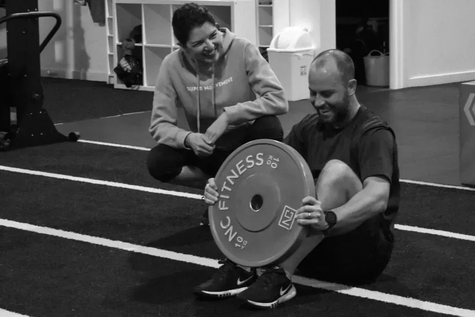 A man is kneeling down holding a weight plate that says fitness on it