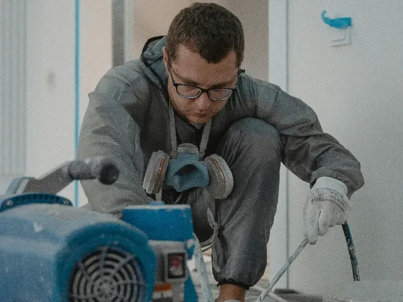 Technician in gray hoodie sanding a surface with a power tool in a workshop
