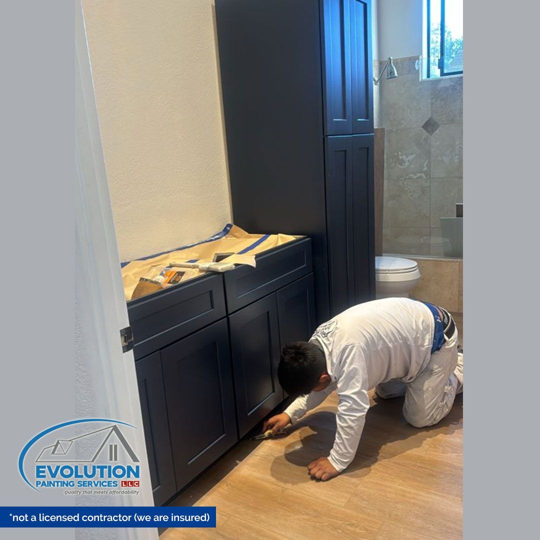 Worker installing cabinet base in a bathroom with dark vanity and tile shower.
