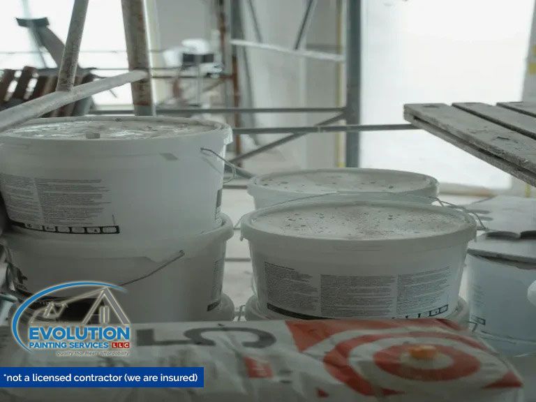 White paint buckets and supplies on a worksite floor with scaffolding in the background