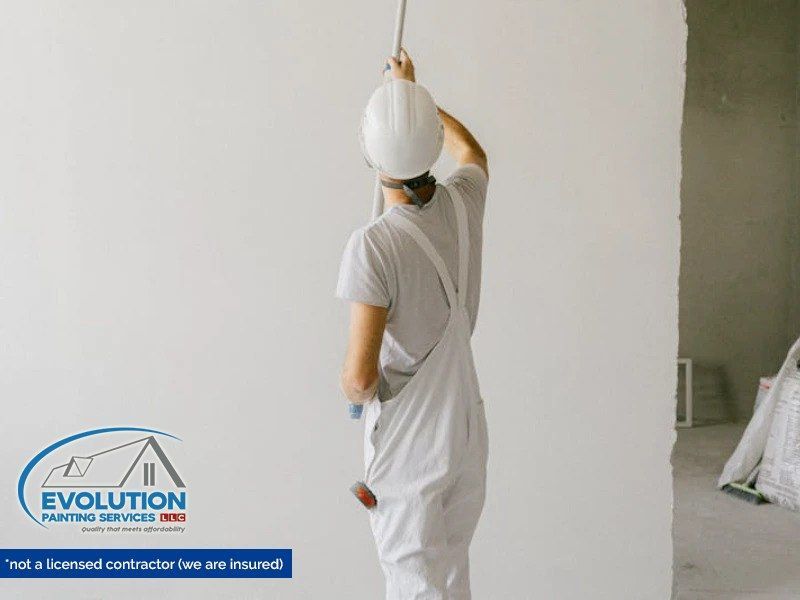 Person in white workwear painting a wall with a roller in a room under renovation.
