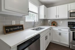 Bright white kitchen with gray tile backsplash, black dishwasher, and a window above the sink.