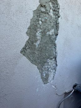 Close-up of a cracked white concrete wall with a jagged dark fissure running across it