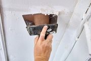 Hand holding a putty knife scraping paint from a white wall patch