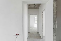 Unfinished white hallway in a building under construction, with exposed wiring and door openings.
