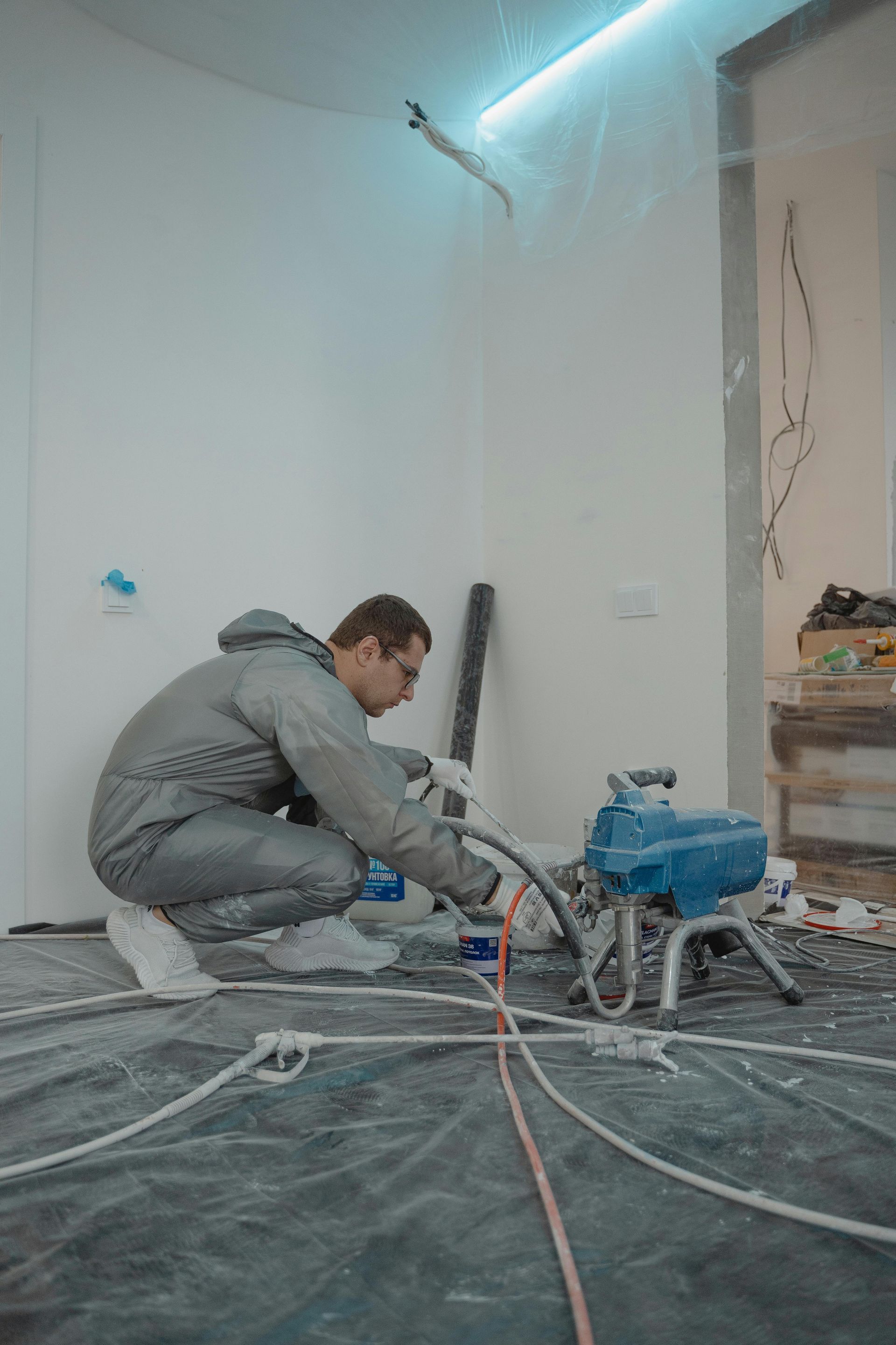 Worker using a floor grinder in a dusty unfinished room with cables and tools on the floor