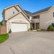 Suburban beige house with double garage and wide driveway under a clear blue sky