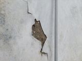 Cracked white wall with a large chipped plaster patch exposing brown underlayer