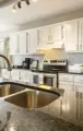 Bright modern kitchen with white cabinets, stainless appliances, and a granite island with sink