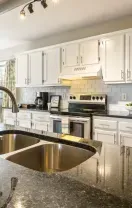 Bright modern kitchen with white cabinets, stainless appliances, and a granite island with sink