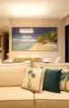 Modern living room with beige sofa, palm-print pillows, dining area, and beach artwork.