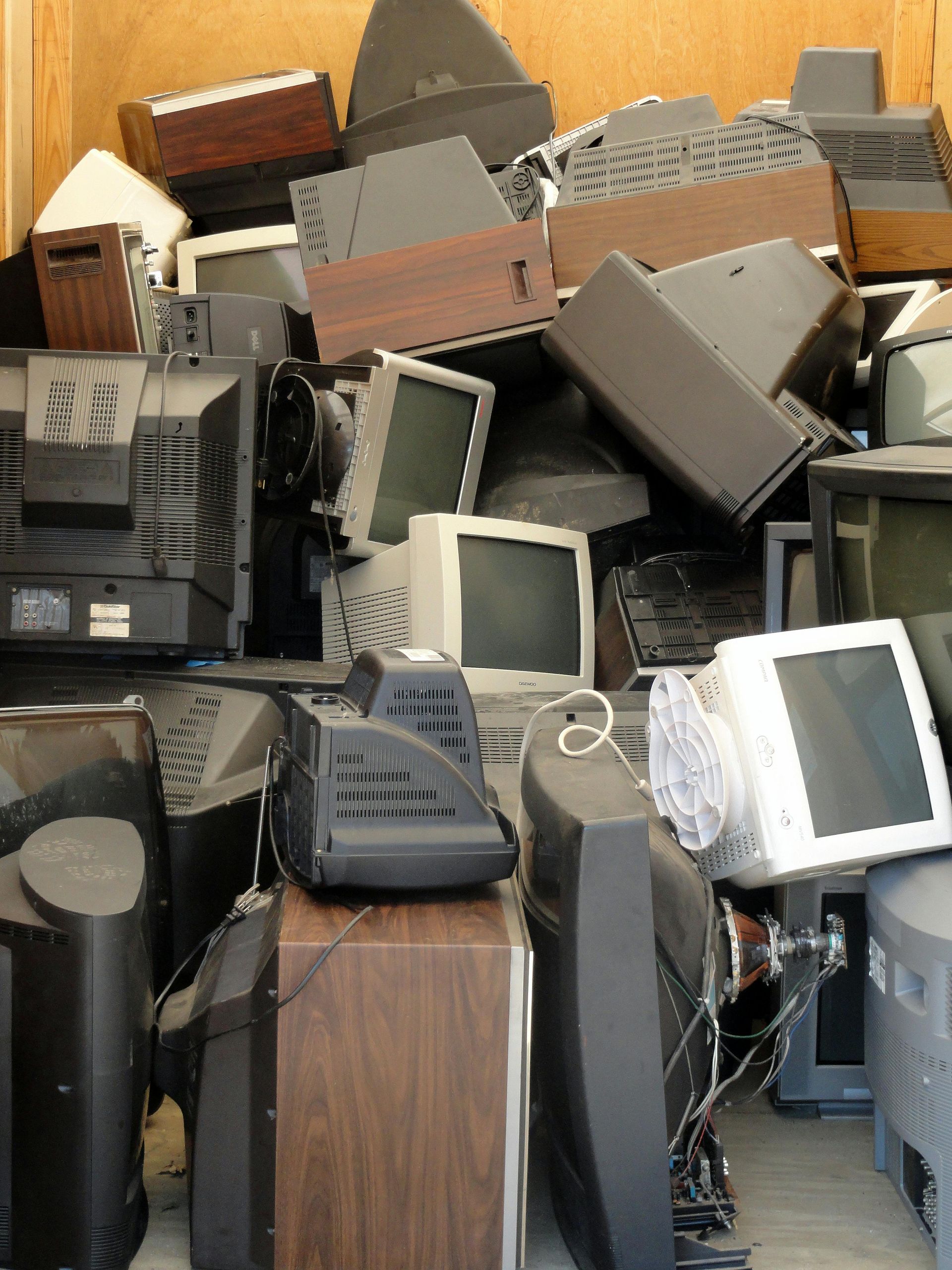 Pile of old computer monitors and televisions in a storage space, ready for disposal.