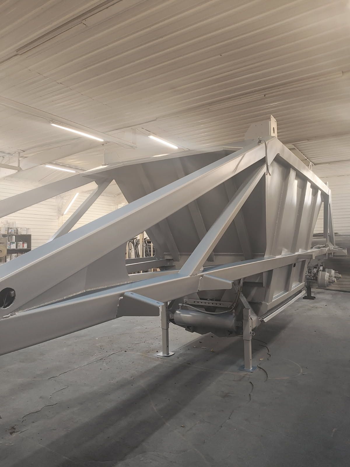 Large gray metal truss structure in a workshop, supported on stands under a corrugated ceiling.