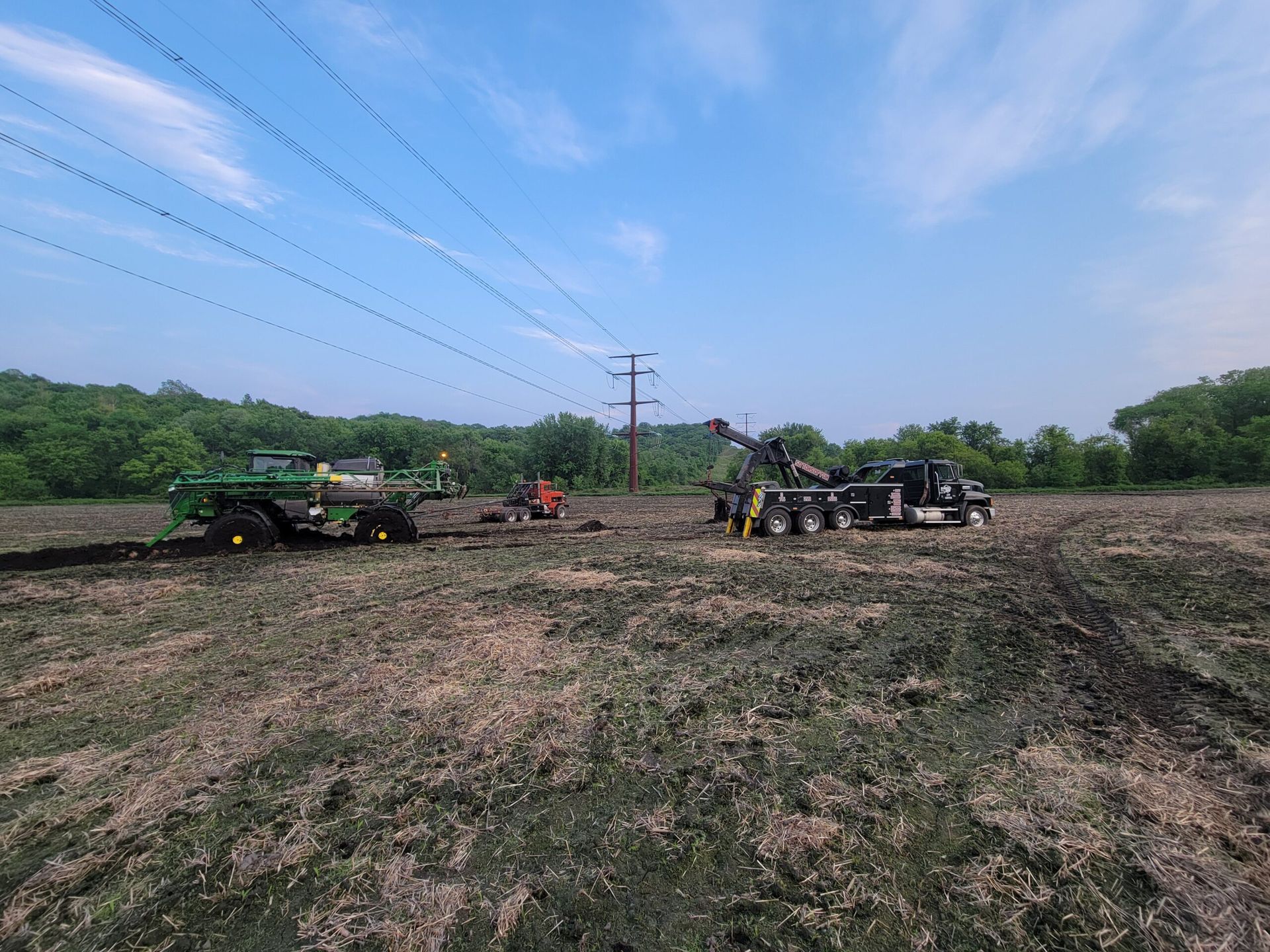 Farm field with several tractors working under a blue sky near power lines